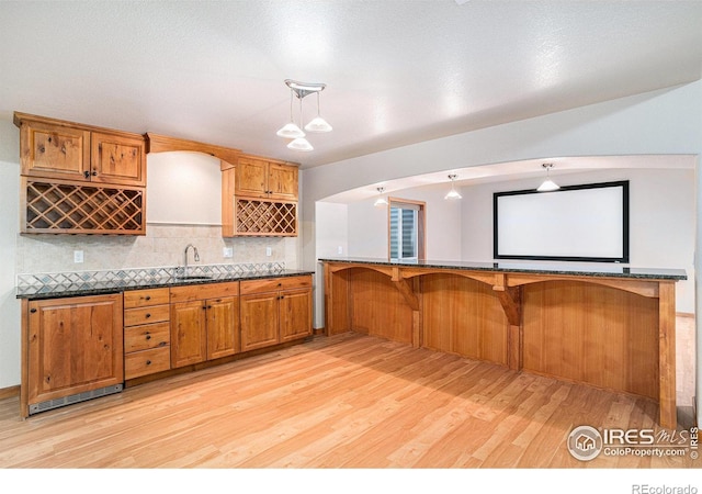 kitchen featuring kitchen peninsula, tasteful backsplash, sink, pendant lighting, and light hardwood / wood-style flooring