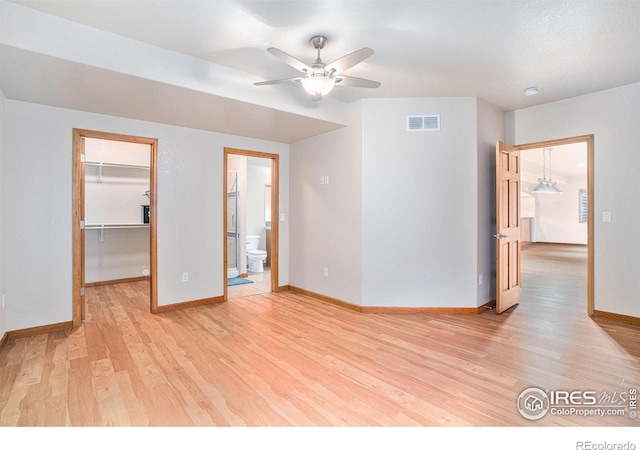 unfurnished bedroom with light wood-type flooring, ensuite bath, ceiling fan, a spacious closet, and a closet