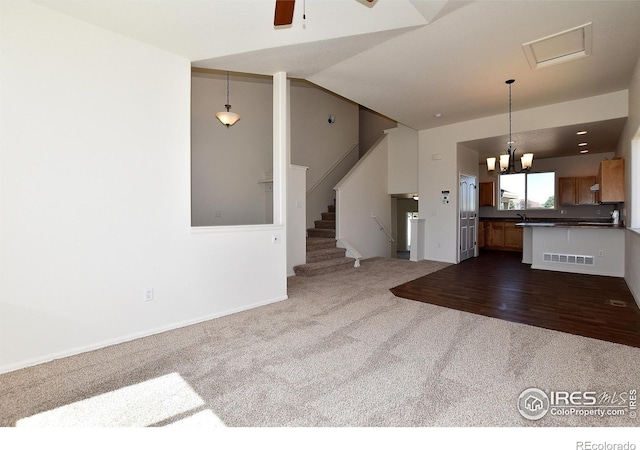unfurnished living room with hardwood / wood-style floors, ceiling fan with notable chandelier, and lofted ceiling