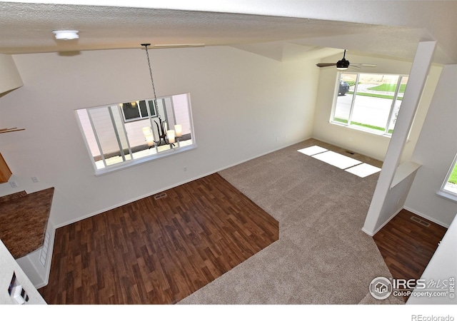 unfurnished living room with dark hardwood / wood-style floors, lofted ceiling, a textured ceiling, and ceiling fan with notable chandelier