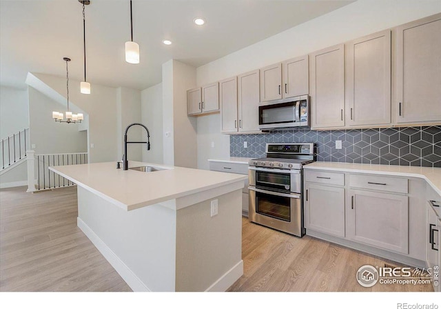 kitchen with sink, light hardwood / wood-style flooring, an island with sink, pendant lighting, and appliances with stainless steel finishes