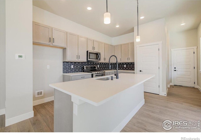 kitchen featuring sink, light hardwood / wood-style flooring, decorative light fixtures, a kitchen island with sink, and appliances with stainless steel finishes