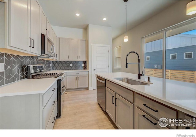 kitchen featuring stainless steel appliances, sink, pendant lighting, a center island with sink, and light hardwood / wood-style flooring