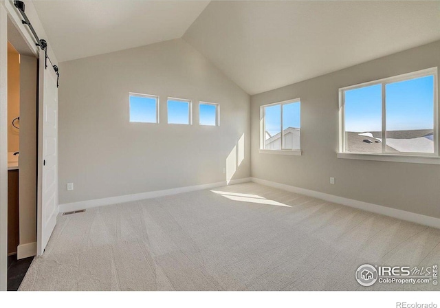 unfurnished bedroom featuring carpet, a barn door, and lofted ceiling