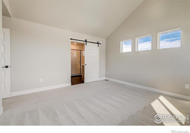 unfurnished bedroom featuring a barn door, carpet floors, and high vaulted ceiling