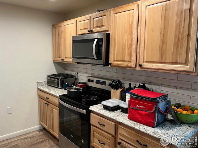 kitchen featuring light hardwood / wood-style flooring, light stone countertops, stainless steel appliances, and tasteful backsplash