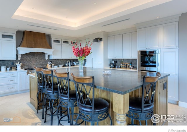 1077 Canyon Blvd # 403, Boulder, CO 80302 - kitchen featuring custom exhaust hood, stainless steel oven, a large island with sink, tasteful backsplash, and white cabinets