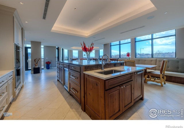 1077 Canyon Blvd # 403, Boulder, CO 80302 - kitchen with a sink, a tray ceiling, stainless steel double oven, a kitchen island with sink, and light stone counters