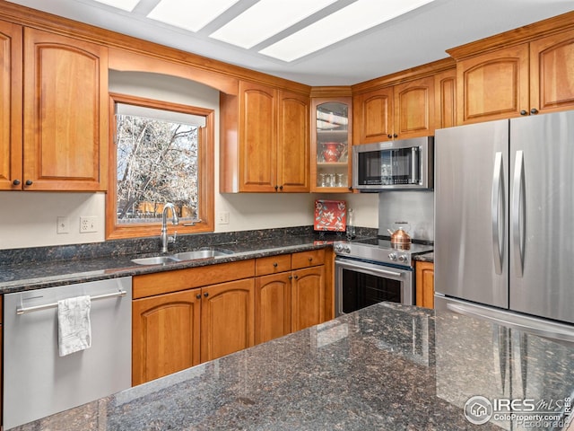 kitchen featuring dark stone countertops, sink, stainless steel appliances, and a skylight