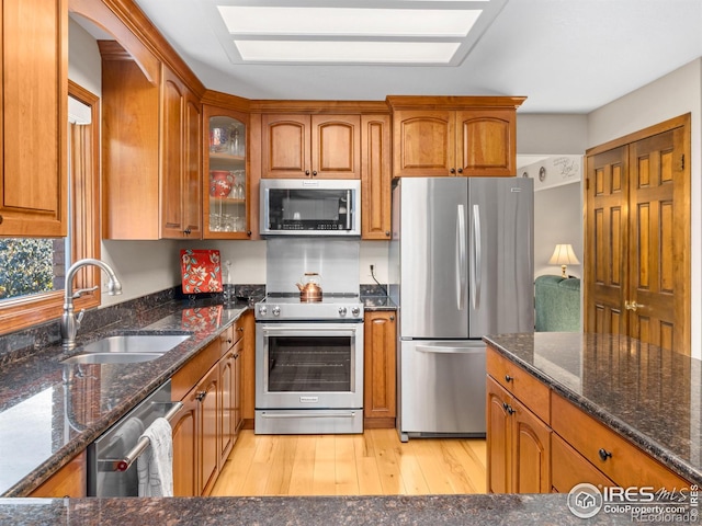 kitchen featuring a skylight, sink, light hardwood / wood-style flooring, dark stone counters, and appliances with stainless steel finishes