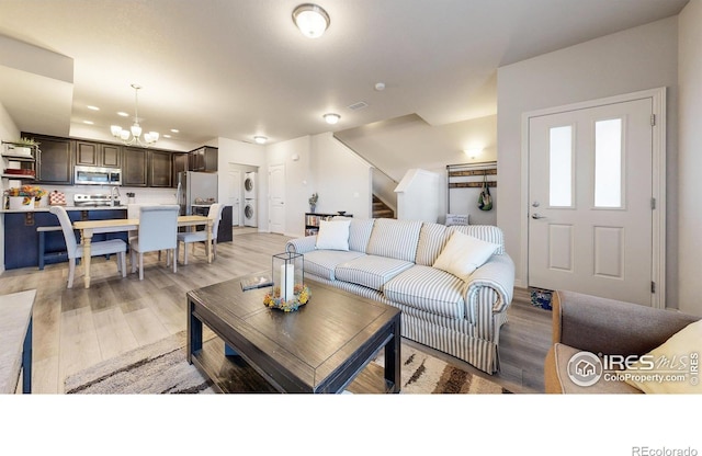 living room with stacked washer and dryer, an inviting chandelier, and light wood-type flooring