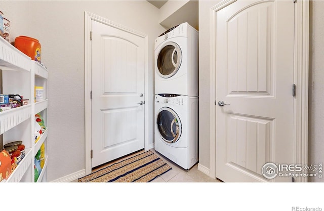 laundry area with stacked washer / drying machine and light tile patterned floors