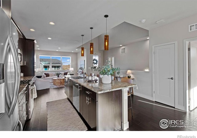 kitchen with pendant lighting, dark brown cabinetry, a kitchen island with sink, and appliances with stainless steel finishes