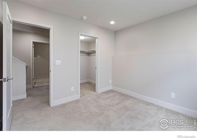 unfurnished bedroom with a walk in closet, a closet, and light colored carpet