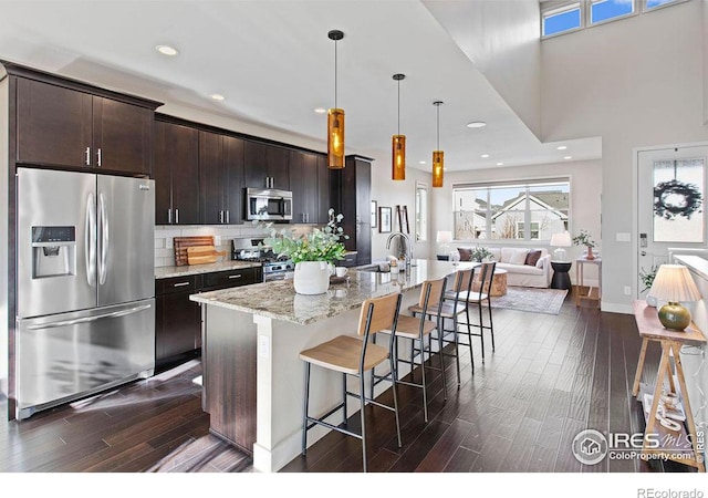 kitchen featuring light stone counters, dark brown cabinets, stainless steel appliances, and a center island with sink