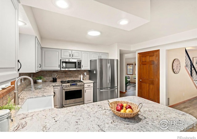 kitchen with sink, light stone countertops, tasteful backsplash, wood-type flooring, and stainless steel appliances