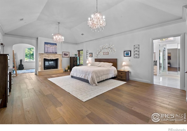 bedroom featuring vaulted ceiling, hardwood / wood-style floors, a notable chandelier, a high end fireplace, and crown molding