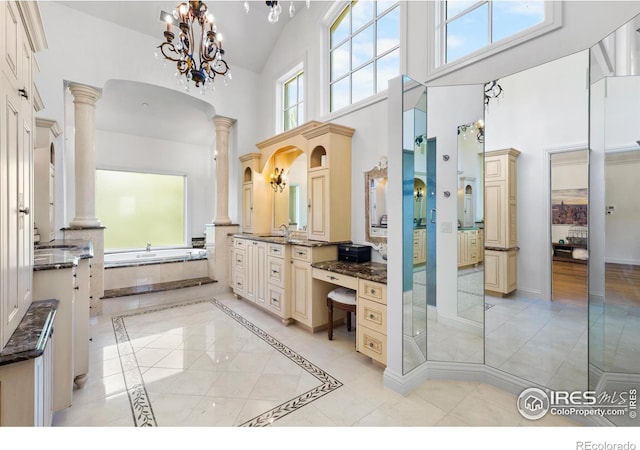 bathroom with decorative columns, a tub to relax in, a high ceiling, vanity, and a notable chandelier