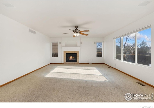 unfurnished living room with a tile fireplace, ceiling fan, and light colored carpet