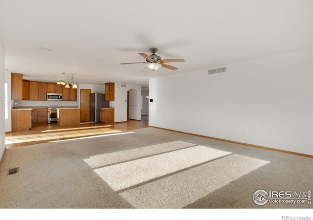 unfurnished living room with light carpet, sink, and ceiling fan with notable chandelier