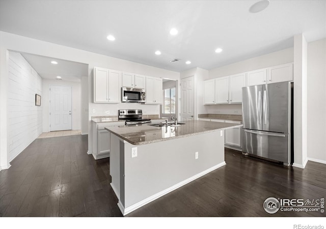 kitchen featuring appliances with stainless steel finishes, light stone counters, white cabinetry, and an island with sink