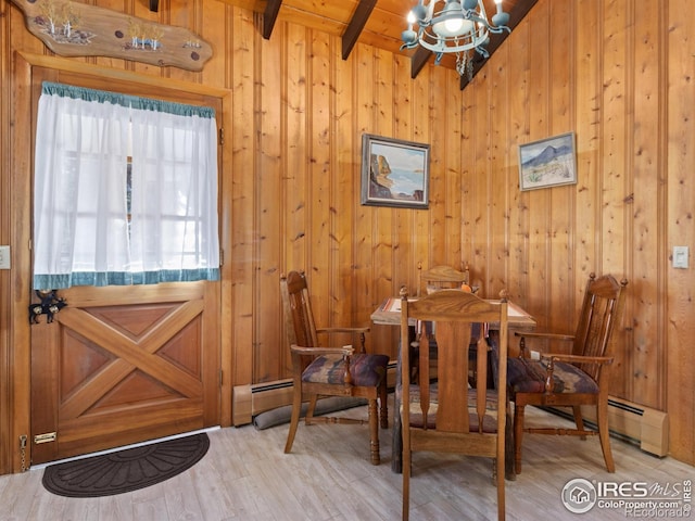 dining space with a baseboard radiator, a chandelier, beamed ceiling, light hardwood / wood-style floors, and wood walls