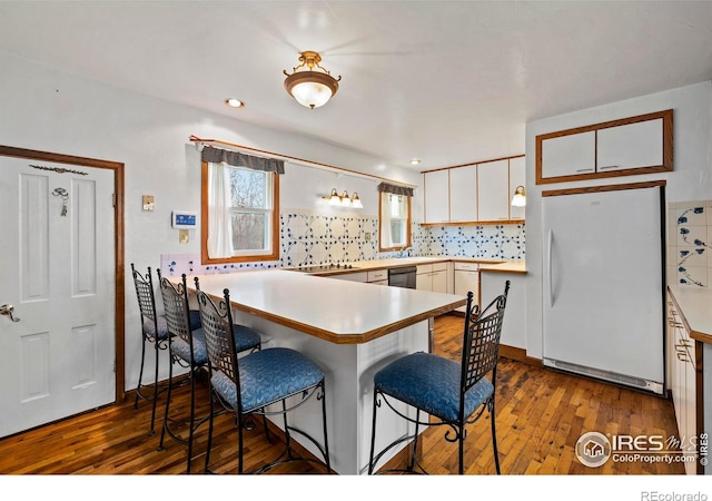 kitchen featuring kitchen peninsula, a breakfast bar, dark wood-type flooring, white fridge, and white cabinetry