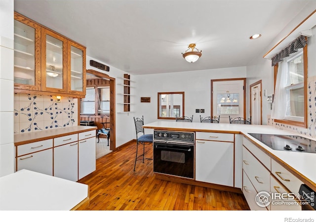 kitchen with white cabinetry, sink, backsplash, black oven, and light wood-type flooring