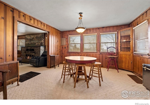 carpeted dining area featuring wood walls, a fireplace, a healthy amount of sunlight, and ornamental molding