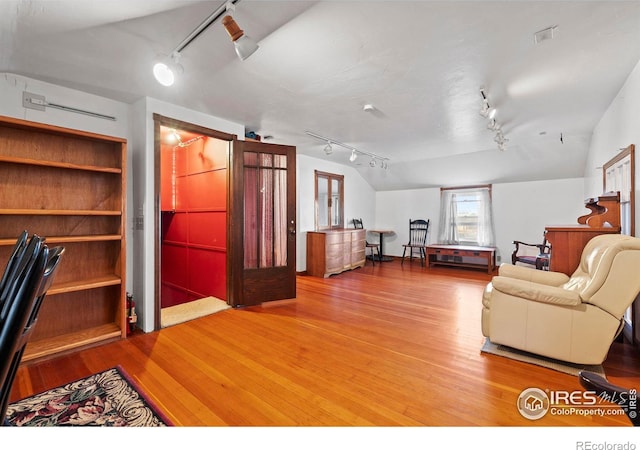 living room with wood-type flooring, rail lighting, and vaulted ceiling