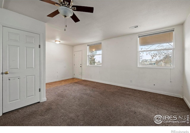 empty room with ceiling fan, a healthy amount of sunlight, a textured ceiling, and dark carpet