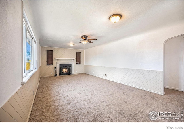 unfurnished living room with carpet, a textured ceiling, ceiling fan, and wooden walls