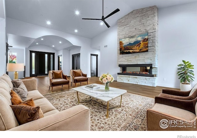 living room with hardwood / wood-style floors, high vaulted ceiling, a stone fireplace, and ceiling fan