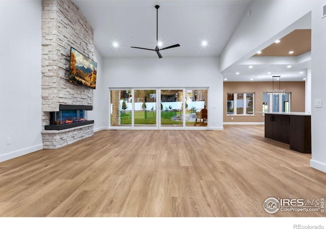 unfurnished living room featuring a fireplace, a towering ceiling, light hardwood / wood-style floors, and ceiling fan