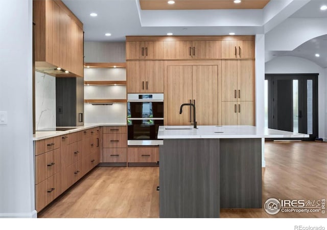 kitchen with an island with sink, light hardwood / wood-style flooring, double oven, and sink