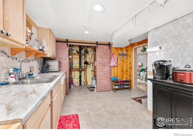 kitchen featuring a barn door, light brown cabinetry, sink, and wooden walls