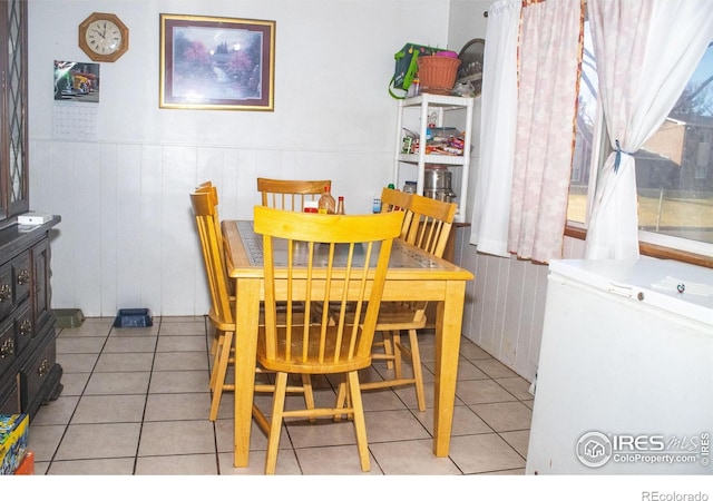 dining space featuring light tile patterned floors and wooden walls