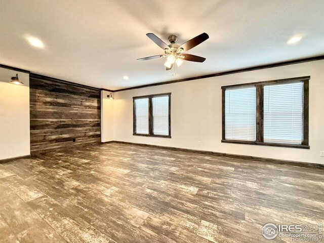 spare room featuring wooden walls, ceiling fan, wood-type flooring, and ornamental molding