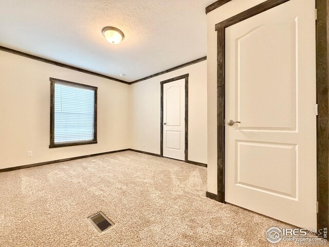 spare room with ornamental molding, a textured ceiling, and light carpet