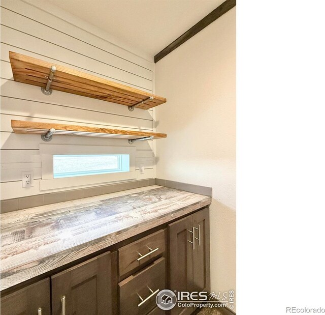 bar with light stone counters, dark brown cabinetry, and ornamental molding