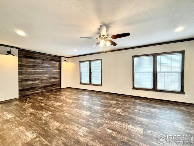 empty room featuring wooden walls, ceiling fan, dark wood-type flooring, and a wealth of natural light