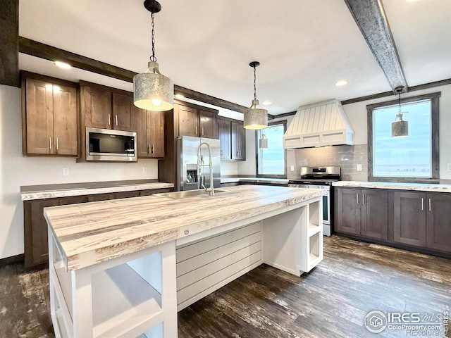 kitchen featuring wood counters, premium range hood, a kitchen island with sink, beamed ceiling, and stainless steel appliances