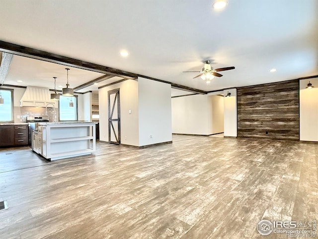 unfurnished living room featuring ceiling fan, beamed ceiling, wood walls, and light wood-type flooring