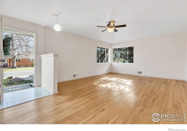 empty room with visible vents, a healthy amount of sunlight, a ceiling fan, and wood finished floors