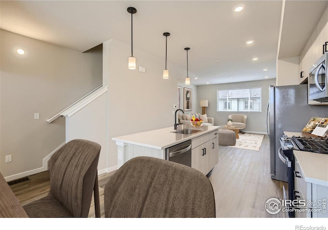 kitchen featuring appliances with stainless steel finishes, light wood-type flooring, a kitchen island with sink, sink, and white cabinetry