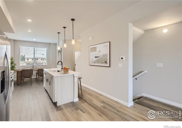 kitchen featuring appliances with stainless steel finishes, sink, a center island with sink, light hardwood / wood-style floors, and hanging light fixtures