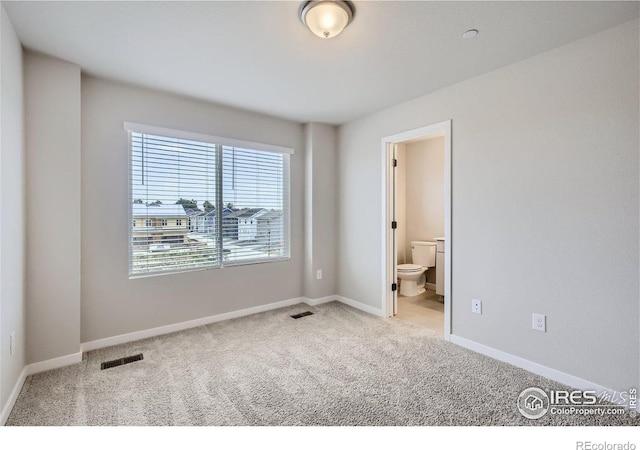 unfurnished bedroom featuring light colored carpet and ensuite bath