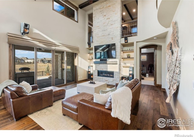 living room with a fireplace, beamed ceiling, wood-type flooring, and a high ceiling