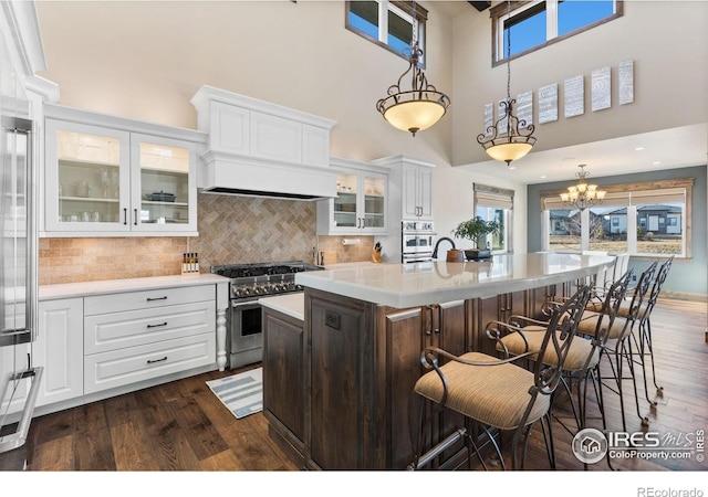 kitchen featuring white cabinets, decorative light fixtures, stainless steel stove, and an island with sink