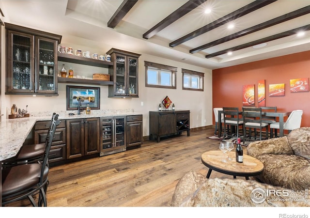 bar with dark brown cabinets, light wood-type flooring, light stone counters, and beverage cooler